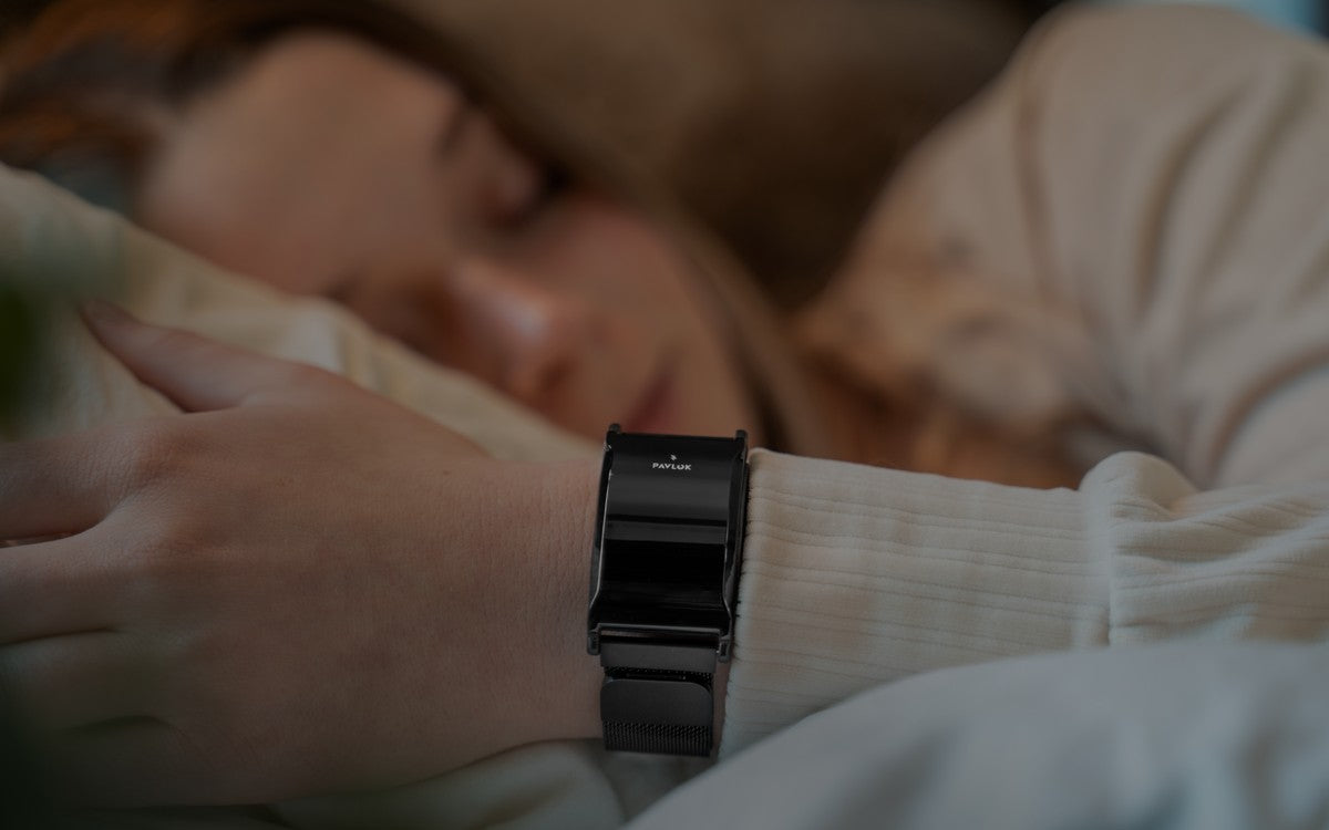 A person's wrist wearing a Pavlok device, seated outdoors in a relaxed pose, face out of frame.